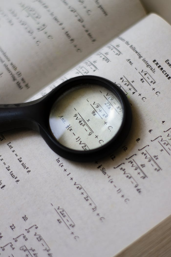gallery-6 A magnifying glass focuses on mathematical equations in a textbook, highlighting detailed calculations.