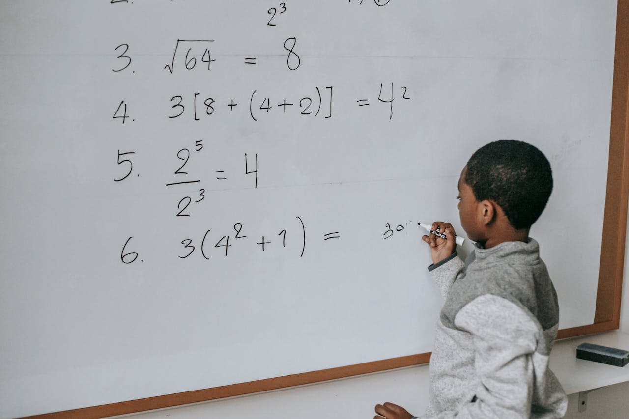 gallery-4 Side view of concentrated African American pupil standing near whiteboard in classroom and solving math examples during lesson at school