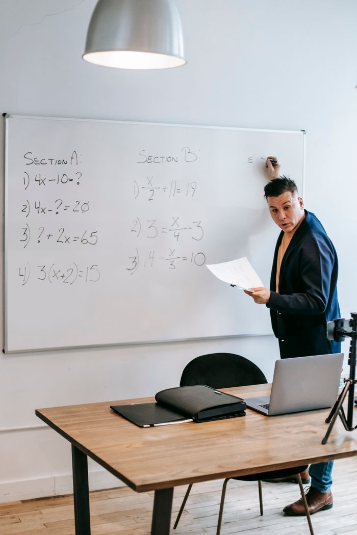 gallery-3 Math instructor teaches equations on a whiteboard using a laptop and tripod setup.