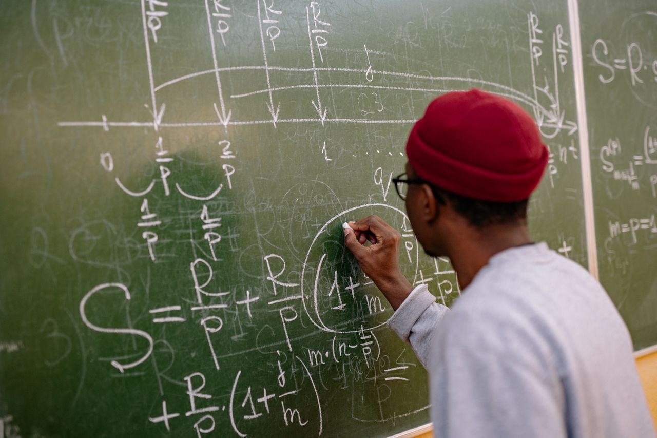 why-choose-us Student writing complex mathematical equations on a chalkboard in a classroom setting.