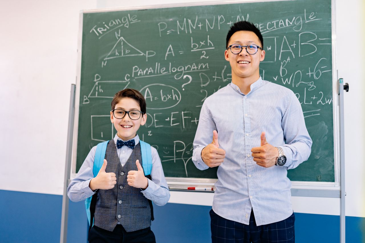 services-01 A teacher and student smiling in front of a chalkboard with mathematical formulas, both giving thumbs up.