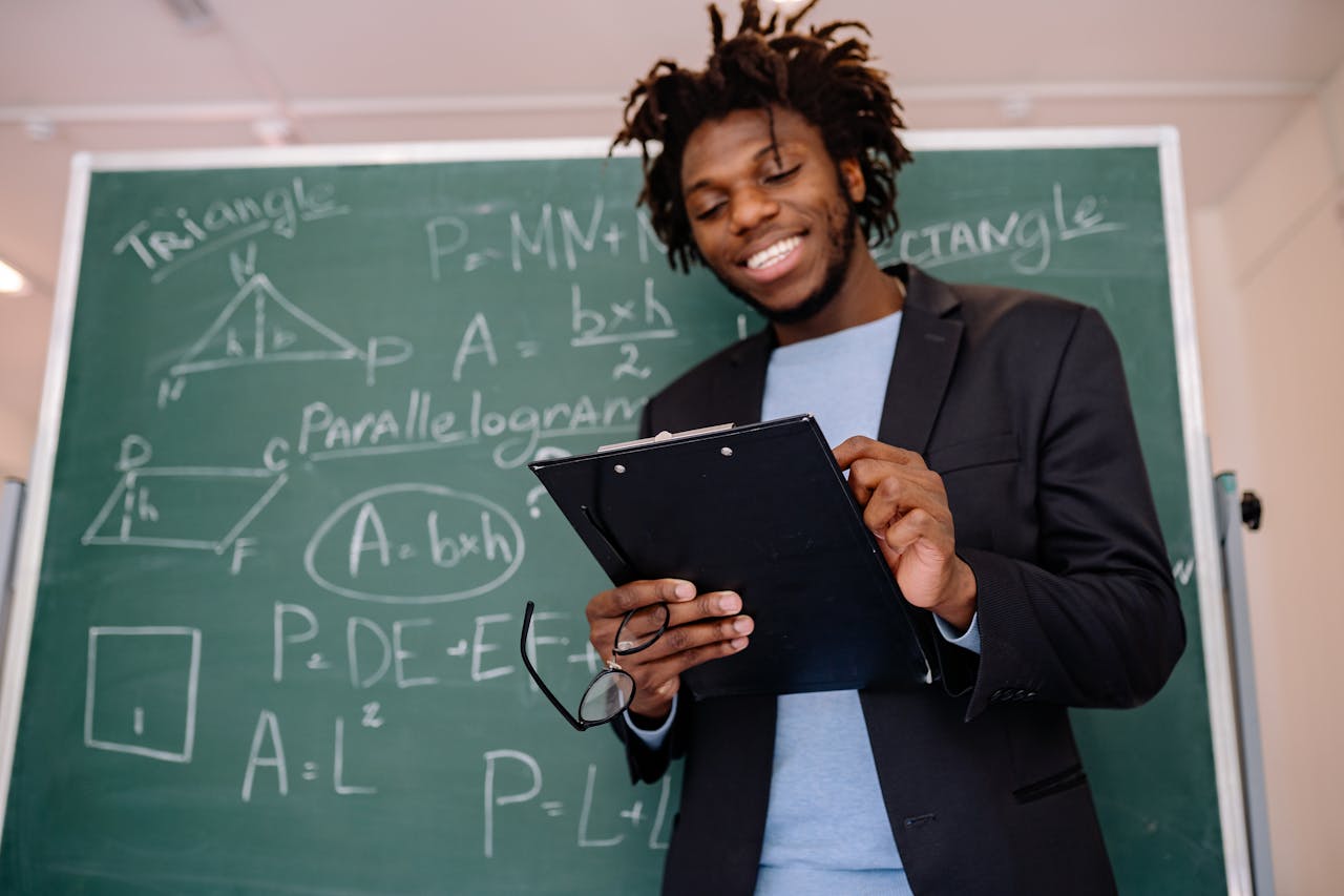 services-02 A happy teacher standing in front of a blackboard with geometric formulas, holding a clipboard.